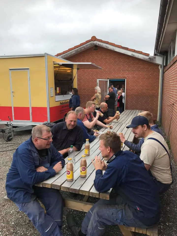 Gæster nyder maden sammen ved langbord foran pølsevognen